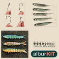 Kit Novato Lago de albur: piezas del kit sobre fondo arena; algunas se muestran con imagen ilustrativa (Anzuelos para vinilo, caja de 50; Vinilos cola en T 7 cm, pack de 5; Swimbait articulado 13,5 cm 19 g; Cabezas jig de tungsteno).